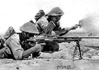 Photograph showing two British troops lying on the ground aiming machine guns (1942)