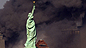 Statue of Liberty in front of smoking buildings
